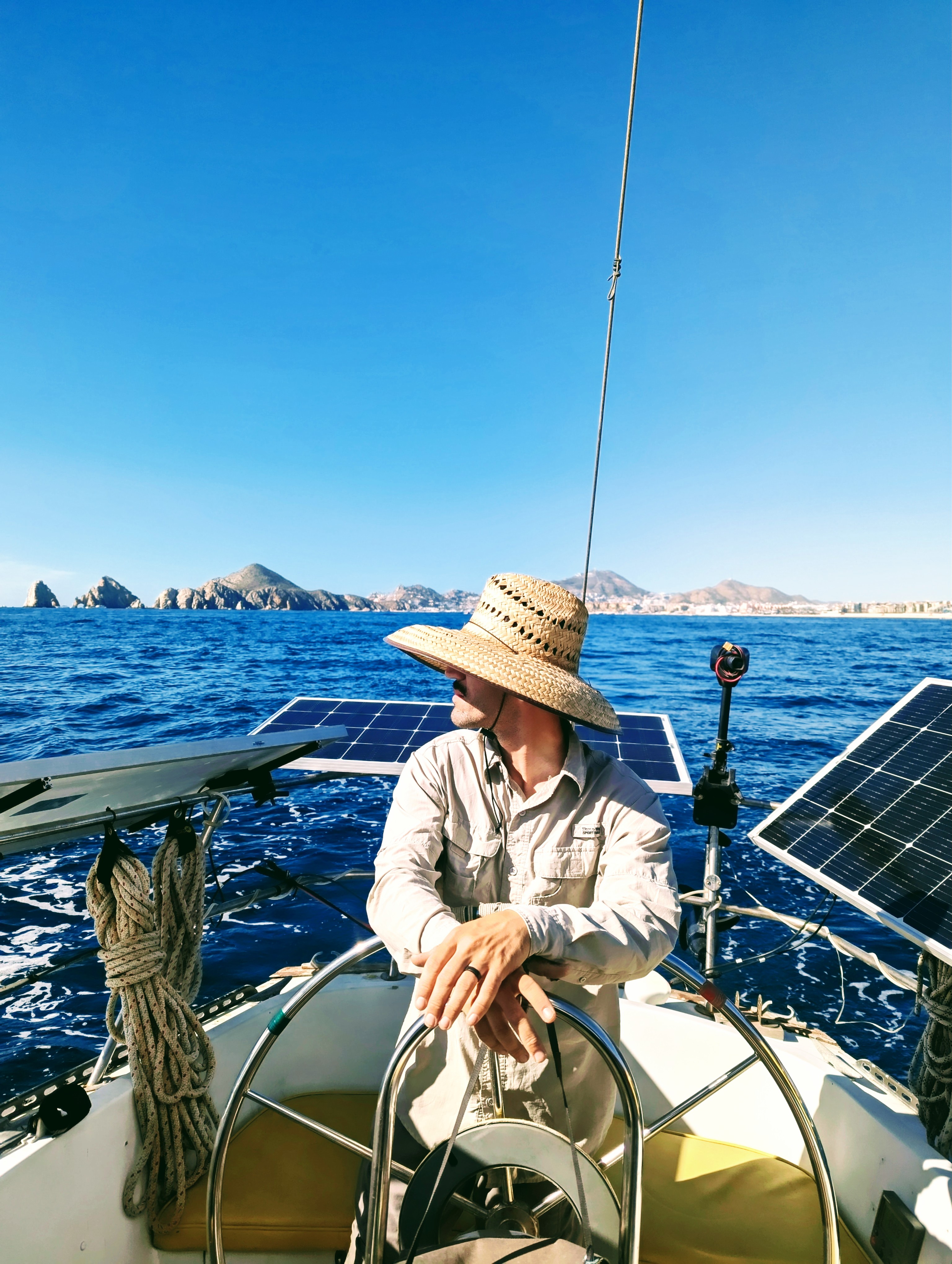 Sailor at the helm wearing a sun hat with solar panels and blue ocean in background