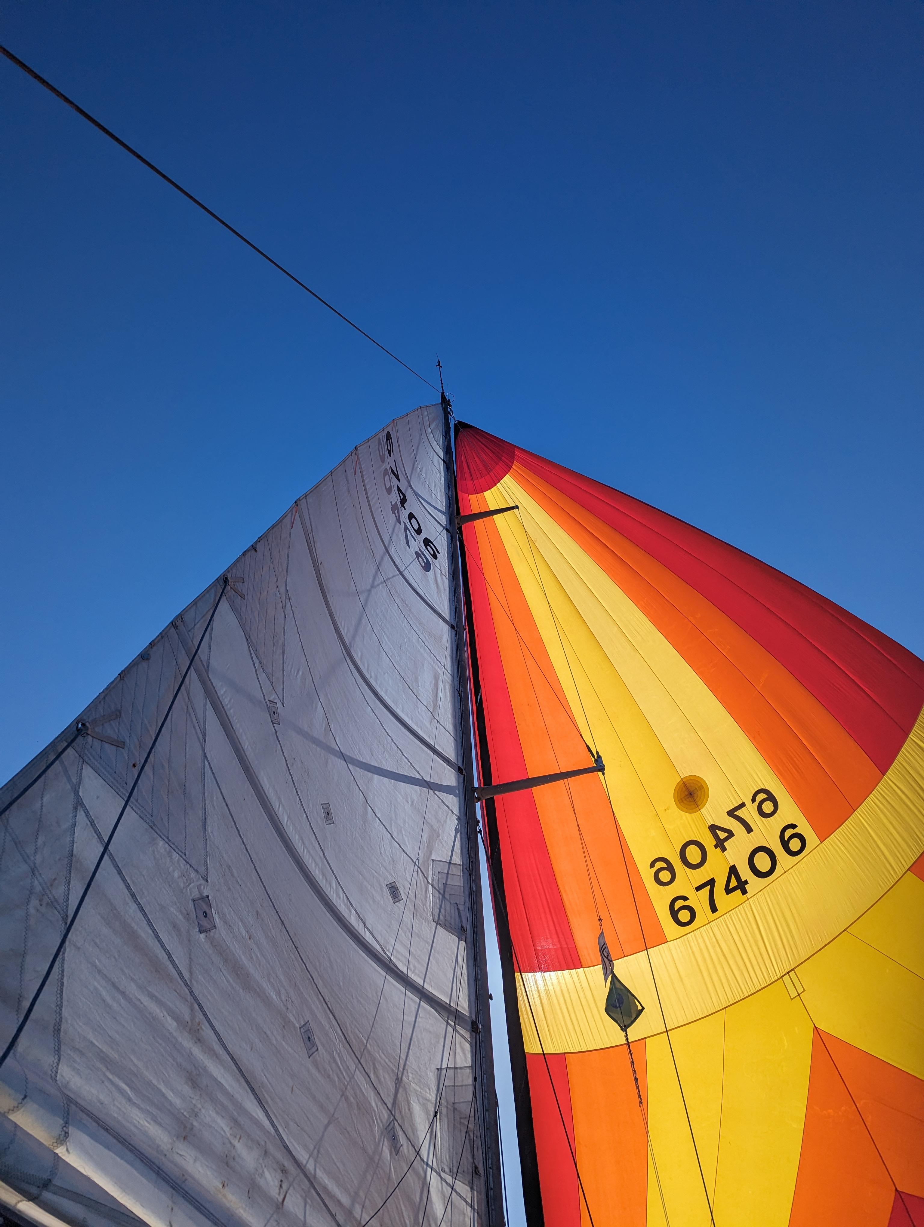 Colorful spinnaker sail with orange, yellow, and red stripes billowing against a clear blue sky