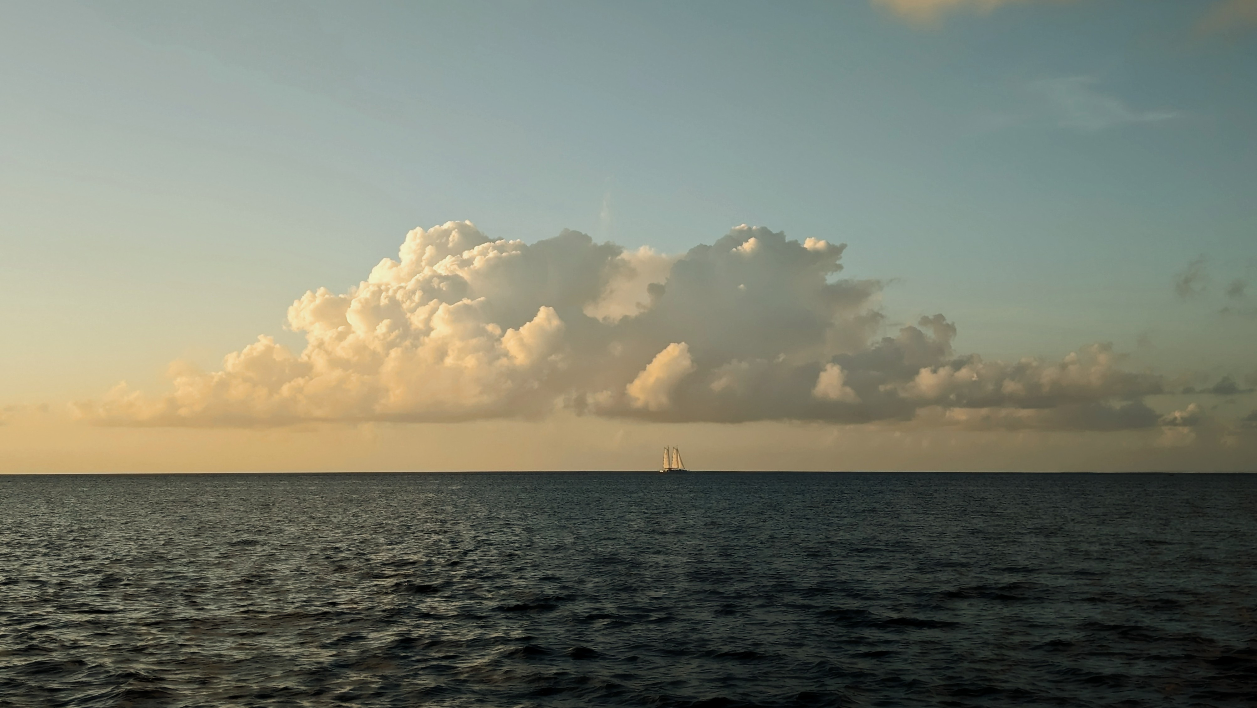 Distant sailboat on the horizon beneath dramatic clouds at dusk