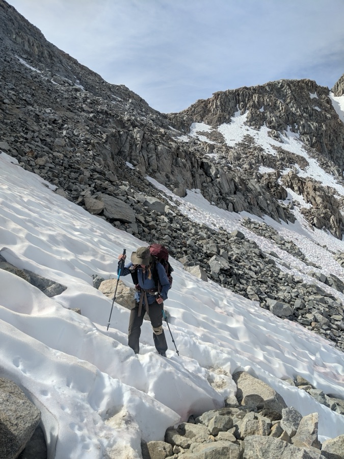 Sam with trekking poles climbing a snowy, rocky mountain slope